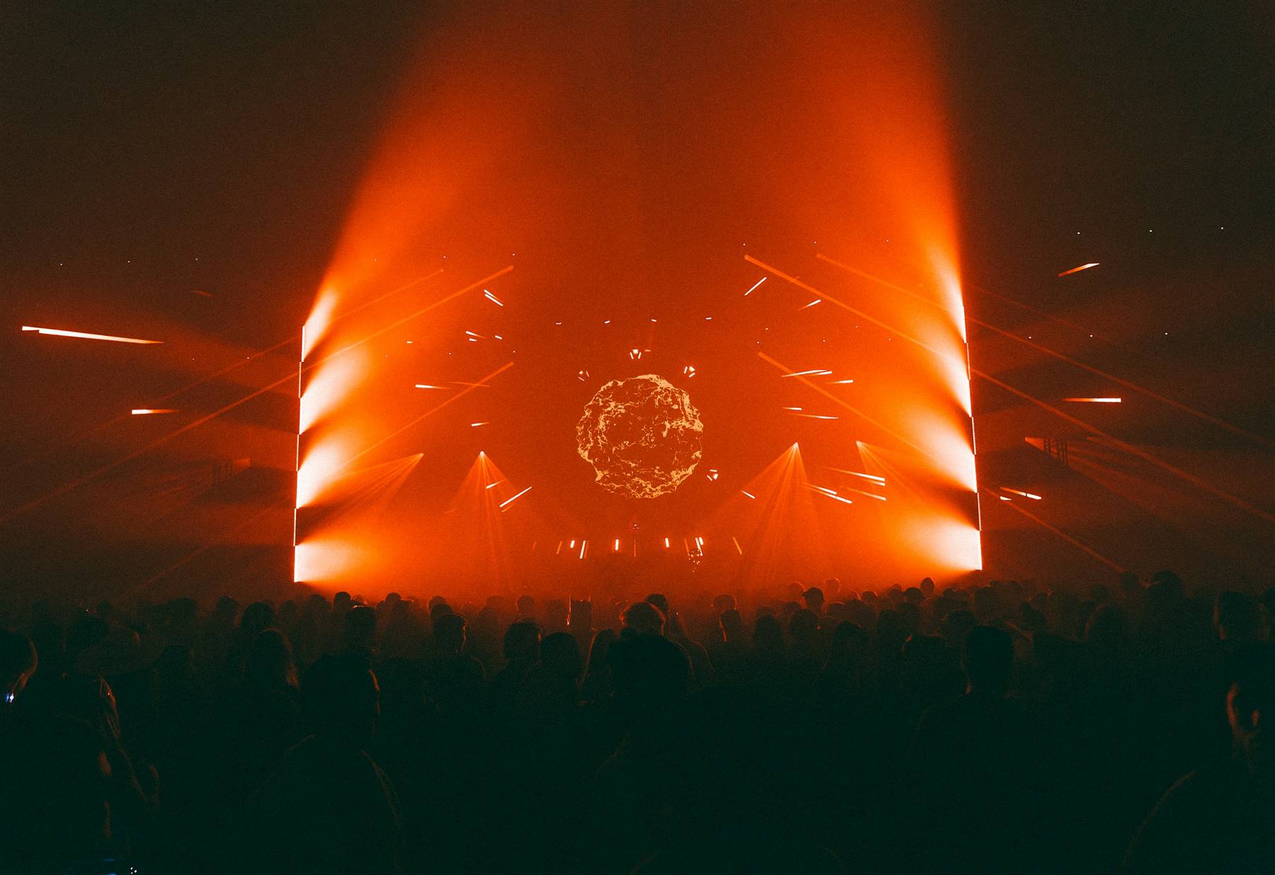A festival crowd facing a stage filled with orange light